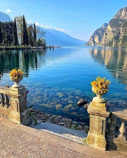 two vases filled with flowers sitting on top of a stone walkway next to the water