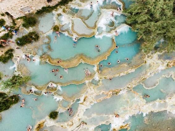 Letecký pohled na Terme di Saturnia, geotermální sírové prameny a přírodní lázně s vodopády v termálních lázních Saturnia. Lidé dávkováním v Cascate del Mulino, Grosseto, Toskánsko, Itálie. — Stock obrázek