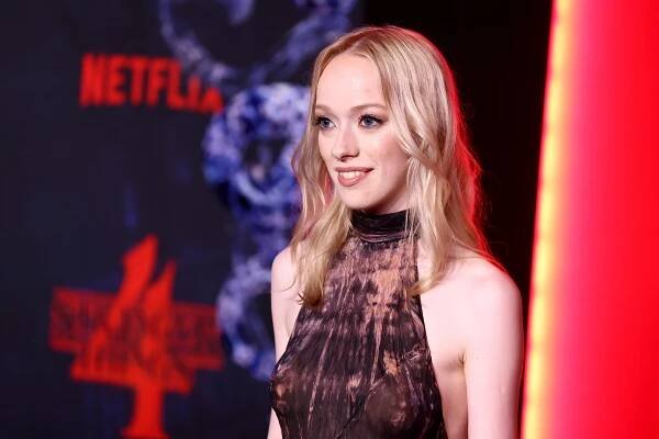Amybeth McNulty Ramírez in tie-dye halter dress at Netflix event with "Stranger Things 4" backdrop, smiling and posing for photos