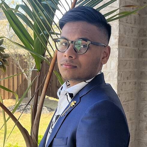 male in blue suit with black rimmed glasses looks at the camera
