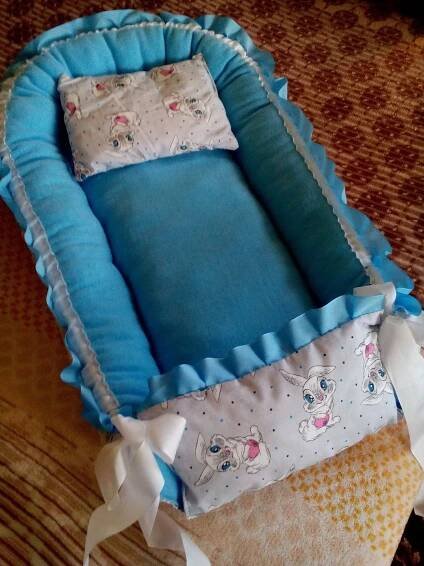 a baby crib with blue and white ruffles on the bottom, in front of a carpeted floor