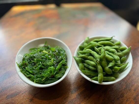 Two bowls of green vegetables are sitting on a wooden table.