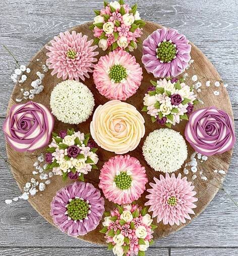 cupcakes decorated with pink and white flowers on a wooden platter, top view