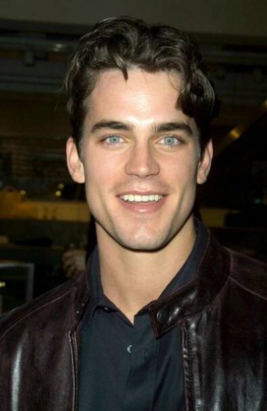 a close up of a person wearing a black shirt and leather jacket smiling at the camera