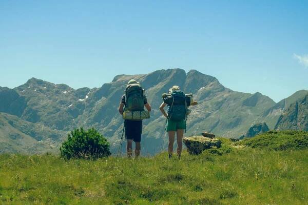 Free Two hikers with backpacks enjoying a mountain view under a clear sky. Stock Photo