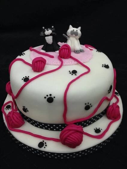 a cake with white frosting and pink icing decorated with black dots, cats on top