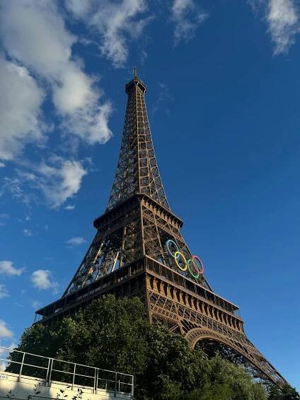 Free View of the Eiffel Tower adorned with Olympic rings against a clear blue sky in Paris. Stock Photo
