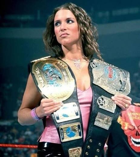 a woman in a pink dress holding two wrestling belts