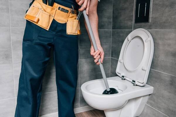 Částečný pohled mužského instalatér pomocí pístu a čištění WC v koupelně — Stock obrázek