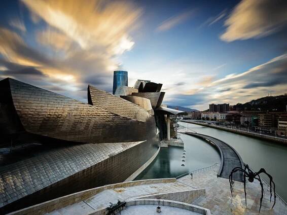 A modern, sculptural building with a flowing river in the background at sunset.