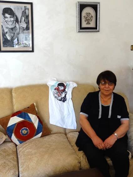 Leila Khaled at her home in Amman, posing with the famous picture of her holding a Kalashnikov rifle, and a T-shirt made by Mlabbas exclusively for her. (Photo: Paula Schmitt)