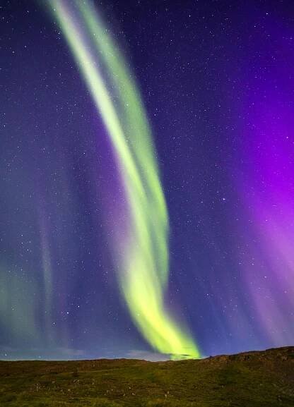 Free Captivating view of aurora borealis dancing over Iceland's night sky with vibrant green and purple hues. Stock Photo
