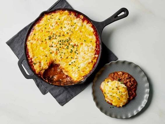 Sloppy Joe Shepherd’s Pie garnished with chives on a plate and in a cast iron skillet 
