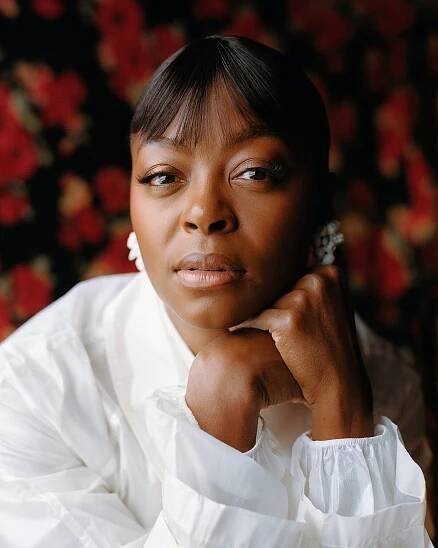A portrait set against a blurred floral background shows a woman in white looking at the camera. Her hands are clasped under her cheek.