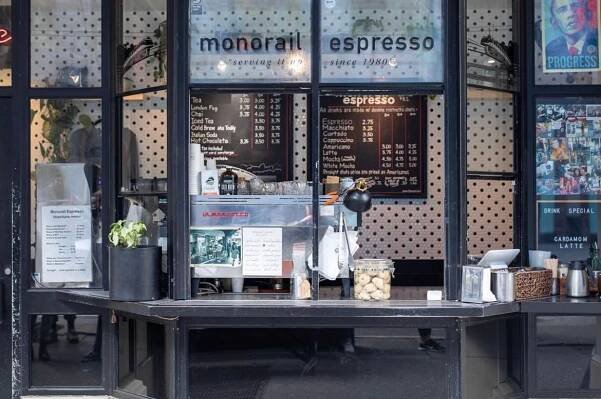 A walk-up cafe window. Behind the glass is an espresso machine. A menu and various other flyers are posted on the windows.