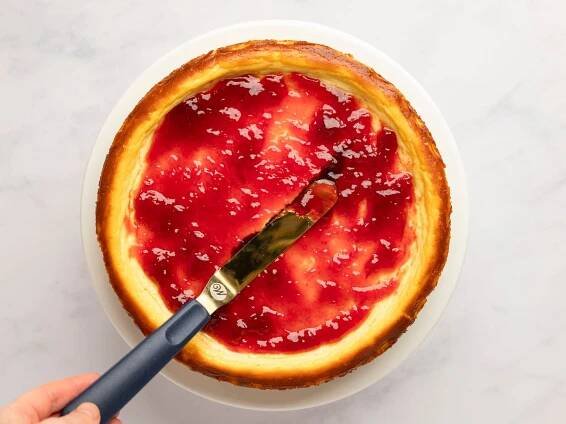 spreading jam over ricotta cheesecake