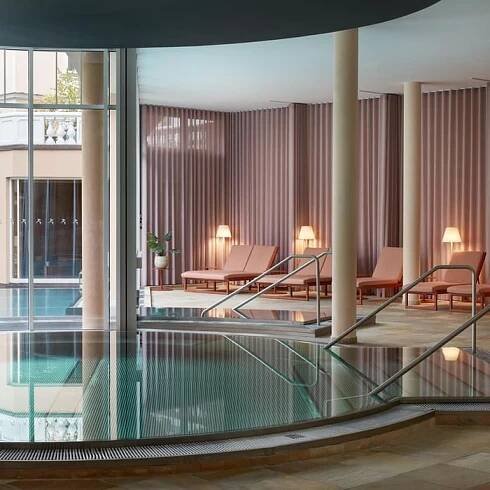 Moderní krytý bazén s prosklenými stěnami, lehátky a sloupy v luxusním wellness centru.