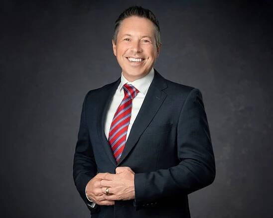 A man in a professional headshot, wearing a suit and tie, poses for a photo.