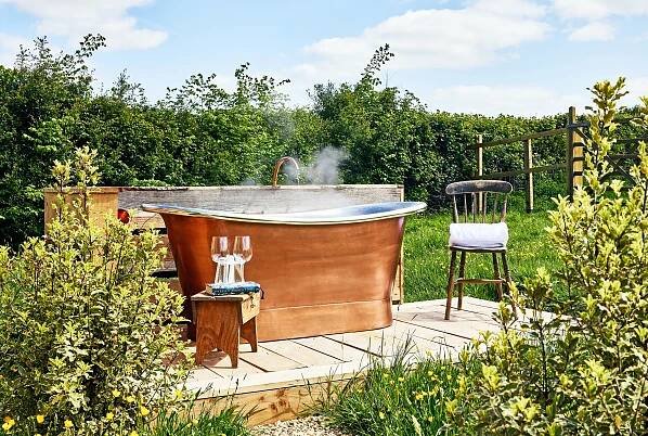Copper bathtub on a wooden deck outdoors.