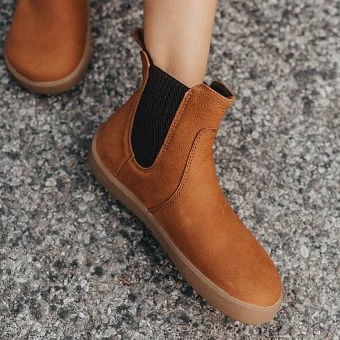 An angled view of a foot resting on concrete wearing Entice Cinnamon Be Lenka barefoot chelsea boots