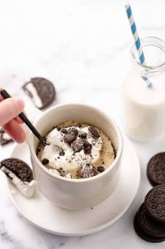 Mug cake with whipped cream and Oreos on top with spoon scooping out a bite