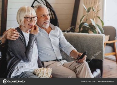 Stáhnout - Starší pár jíst popcorn a dívat se na televizi doma interiér — Stock obrázek