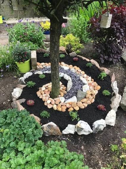a tree in the middle of a garden with rocks and plants around it, surrounded by gravel