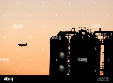 Airplane silhouetted flying past cisterns at early dawning. Stock Photo