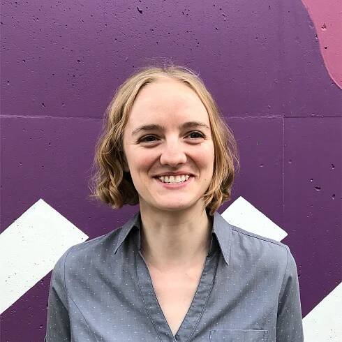 A photo of Kate Kryder in front of a purple, white, and pink wall. 