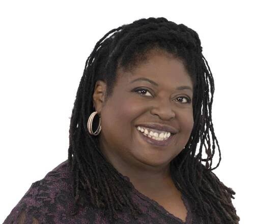 A woman with braids and hoops wearing a purple lace dress smiling at the camera