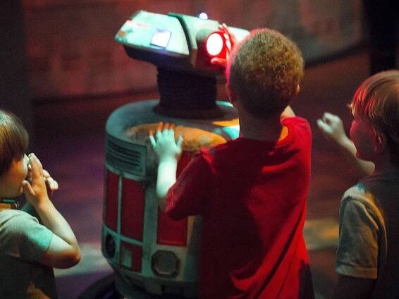 Three children gather around a robot.