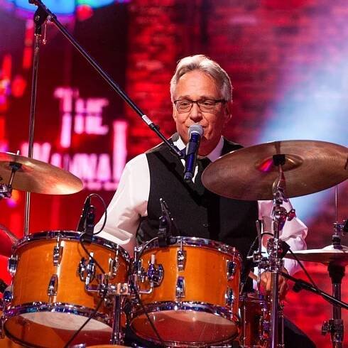 Drummer in glasses performing on stage with a drum kit and microphone.