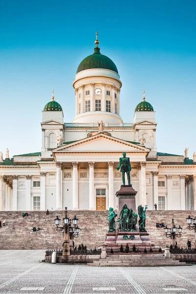A view of Helsinki Cathedral in Finland, featuring its iconic green domes and neoclassical architecture, with the statue of Emperor Alexander II in the foreground at Senate Square.