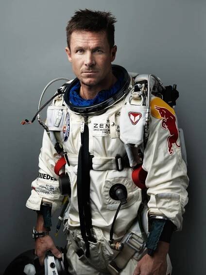 A man holding a helmet and in a white suit is photographed on a grey background.
