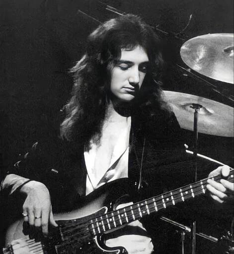 a black and white photo of a man playing the guitar in front of a drum set