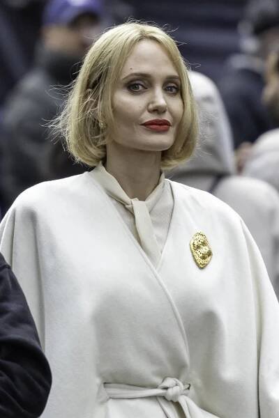 a woman with short blonde hair wearing a cream coat