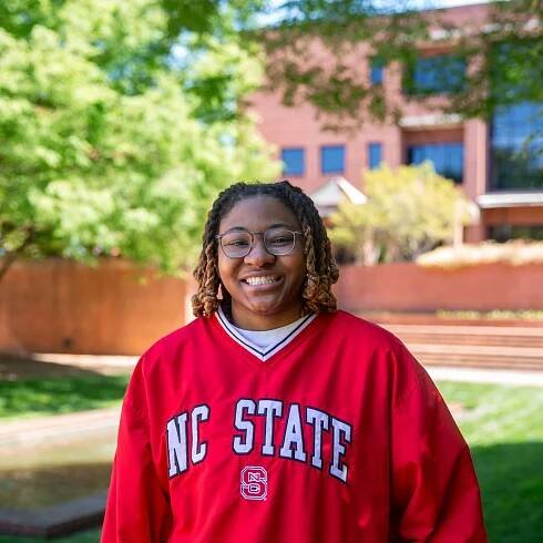 Jordan Everett wears a red NC State pullover. The Wilson College of Textiles and a courtyard is visible behind her.