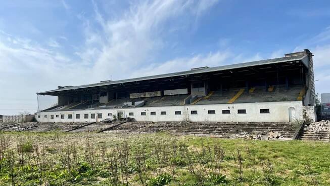 A derelict Casement Park, the grass is overgrown and there is rubble in and around the stand