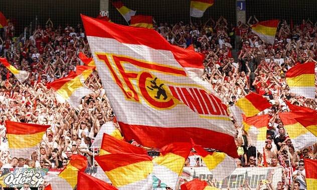 Flaggen des 1. FC Union Berlin werden von begeisterten Fans in einem Stadion geschwenkt.