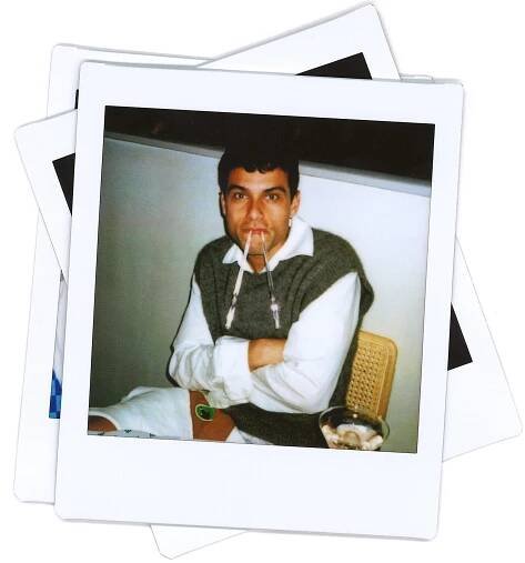 A man seated at a table holds two swizzle sticks in his mouth for comic effect.