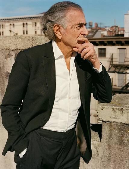 A man, wearing a black suit and a white shirt, stands on a rooftop in New York.