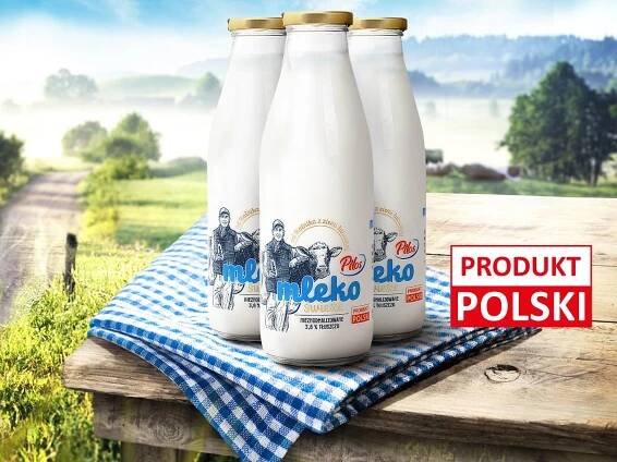 Trzy butelki mleka Pilos na drewnianym stole na tle wiejskiego krajobrazu.