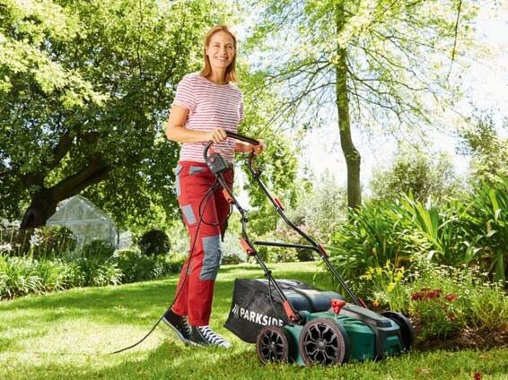 Žena seče trávu elektrickou sekačkou Parkside v zahradě.