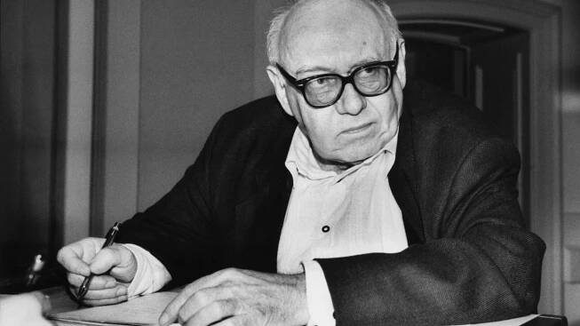 Das Foto zeigt den Dichter Ernst Jandl an einem Tisch sitzend mit Notizblock und Stift in der Hand.