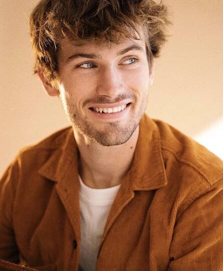 a man smiling and looking at the camera while wearing an orange shirt with his hands on his hips