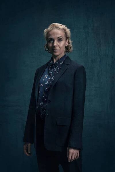a woman standing in front of a dark background wearing a black jacket and floral shirt