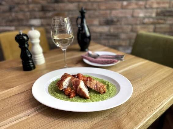 a white plate topped with meat covered in green sauce next to a glass of wine