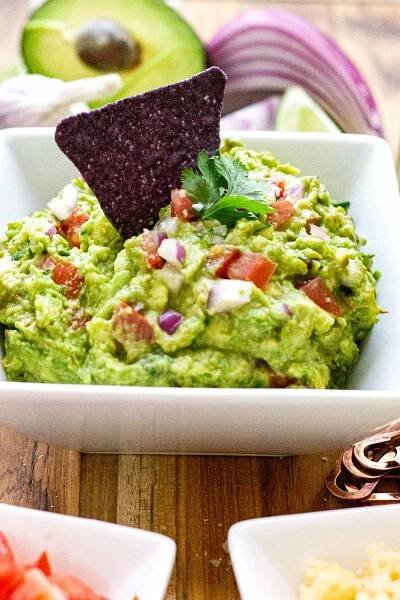 Blue corn chip dipped in guacamole served in a white bowl. 