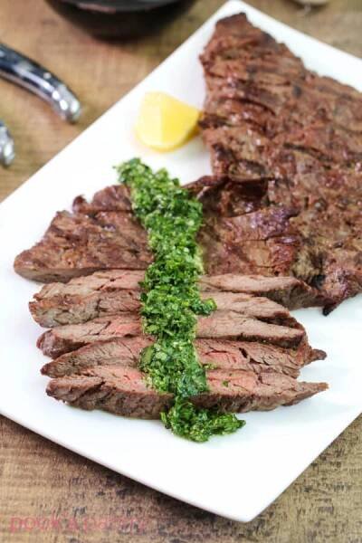 Steak gremolata on white rectangular platter with lemon wedges.