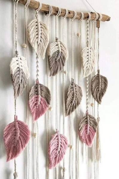 a wall hanging with pink and white feathers on it's side, next to a plant